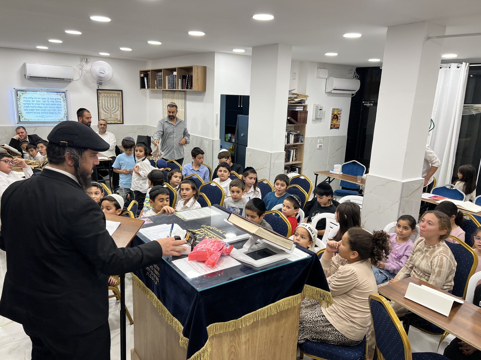 Le Rav s’adresse à une salle comble d’enfants attentifs lors d’un chiour Avot Oubanim