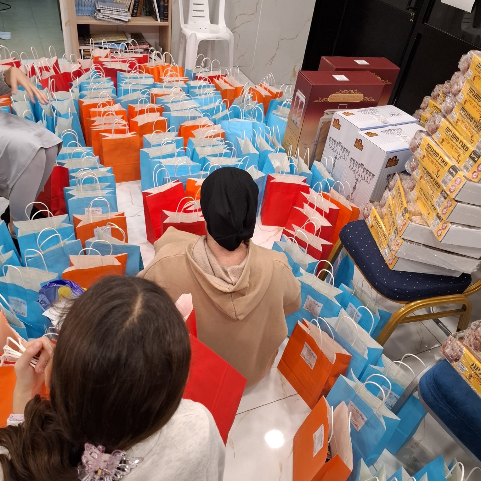 Bénévoles de dos au milieu de dizaines de sacs cadeaux préparés pour les Hayalims