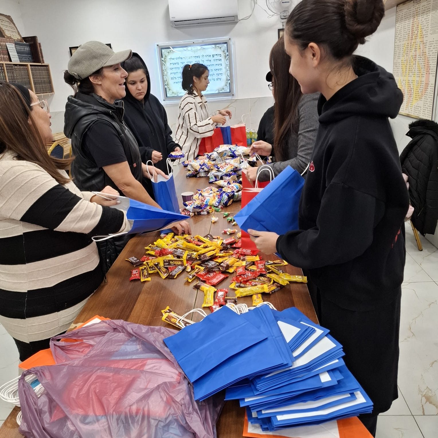 Bénévoles autour d’une table couverte de friandises, remplissant les sacs cadeaux des Hayalims