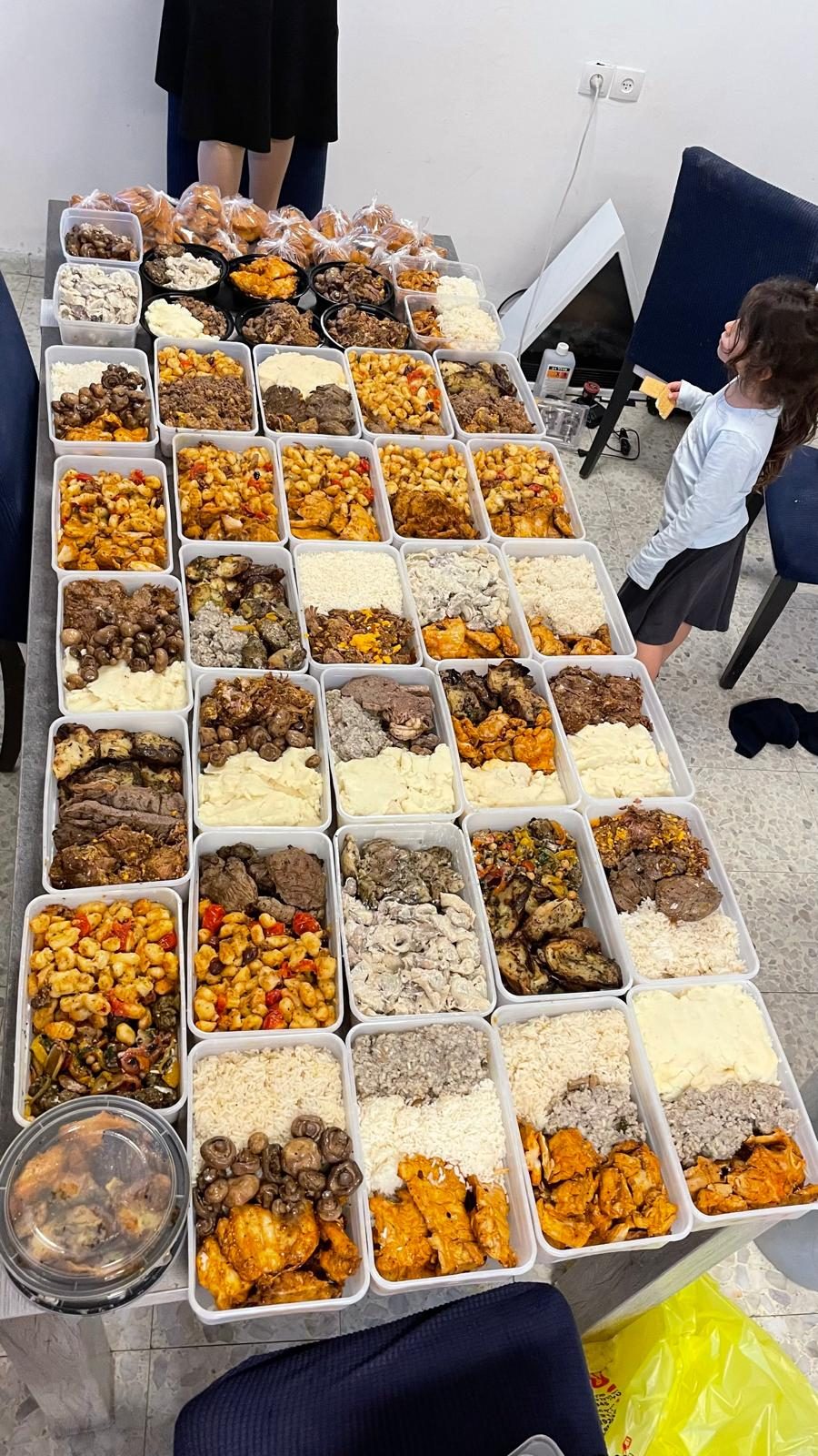 Grande table couverte de dizaines de barquettes-repas préparées par les bénévoles du Hessed